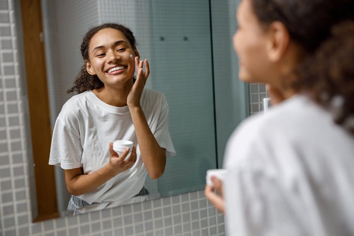 Smiling woman applying anti-wrinkle cream standing behind mirror in home bathroom.High quality photo