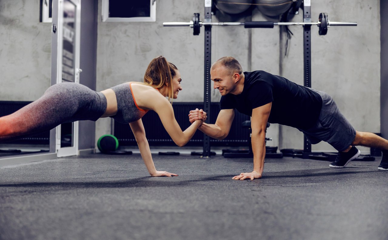Motivation and support in training, sports lifestyle. The couple does sports exercises together. They are in push ups position and holding hands to maintain body balance. Fitness challenge