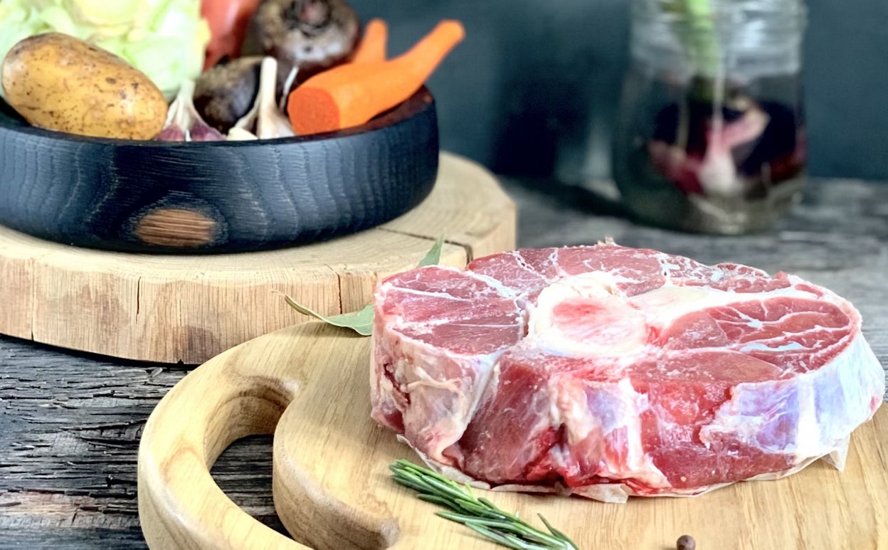A piece of meat on a cutting board next to vegetables