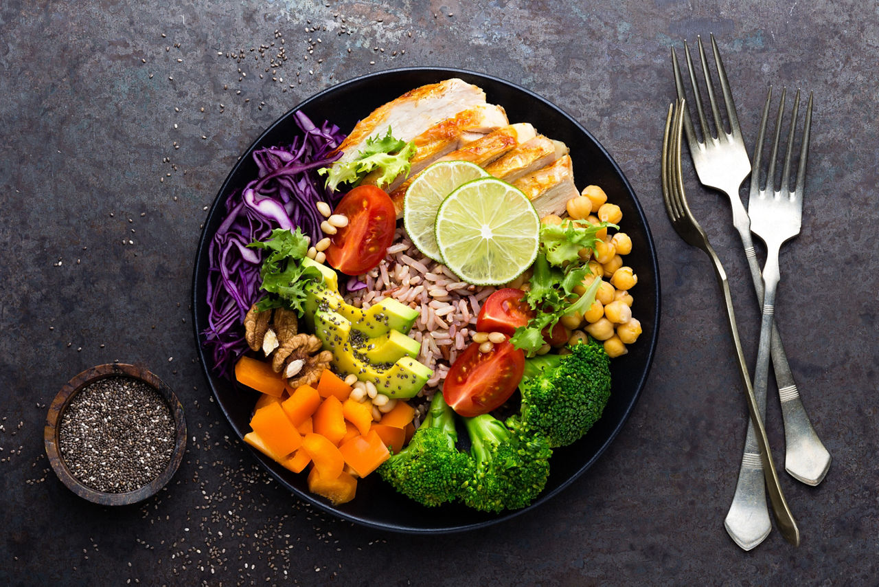 Buddha bowl dish with chicken fillet, brown rice, avocado, pepper, tomato, broccoli, red cabbage, chickpea, fresh lettuce salad, pine nuts and walnuts. Healthy balanced eating.