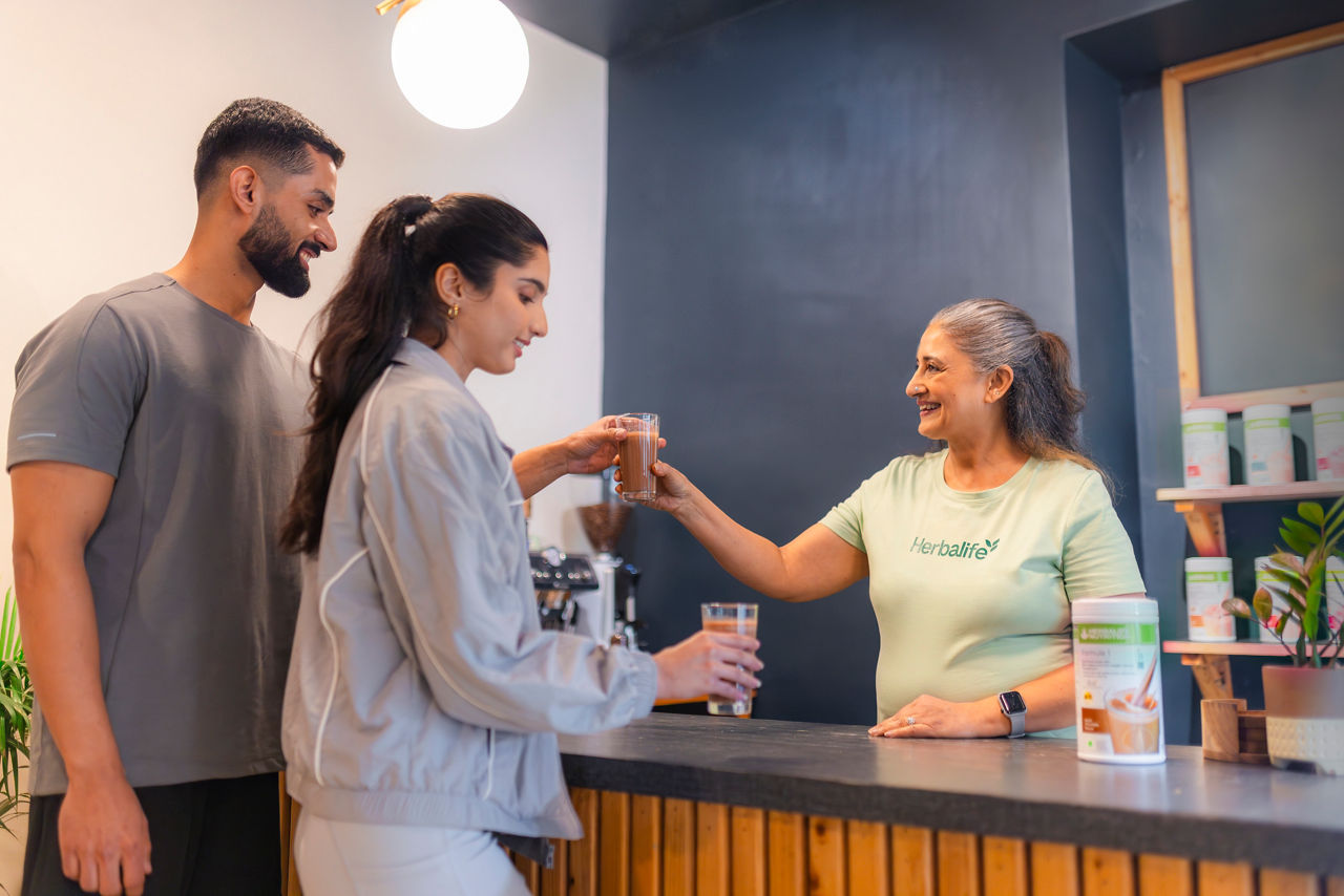 A smiley woman serving Formula 1 shakes to a couple at a Nutrition Club