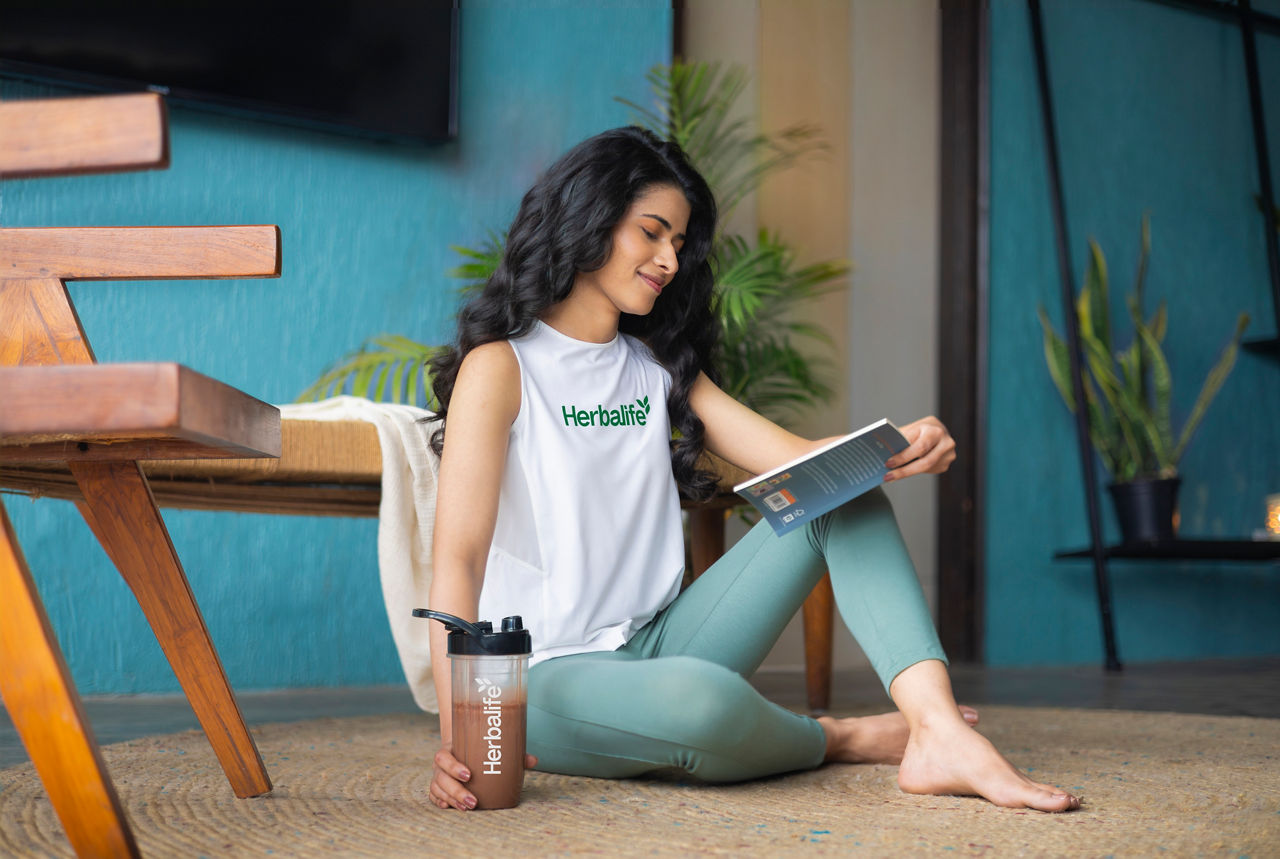 Woman reading a book at home and holding a shaker with chocolate shake