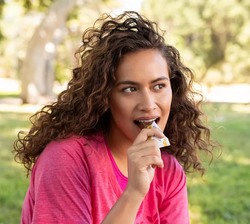 Femme mangeant une barre protéinée dans un parc