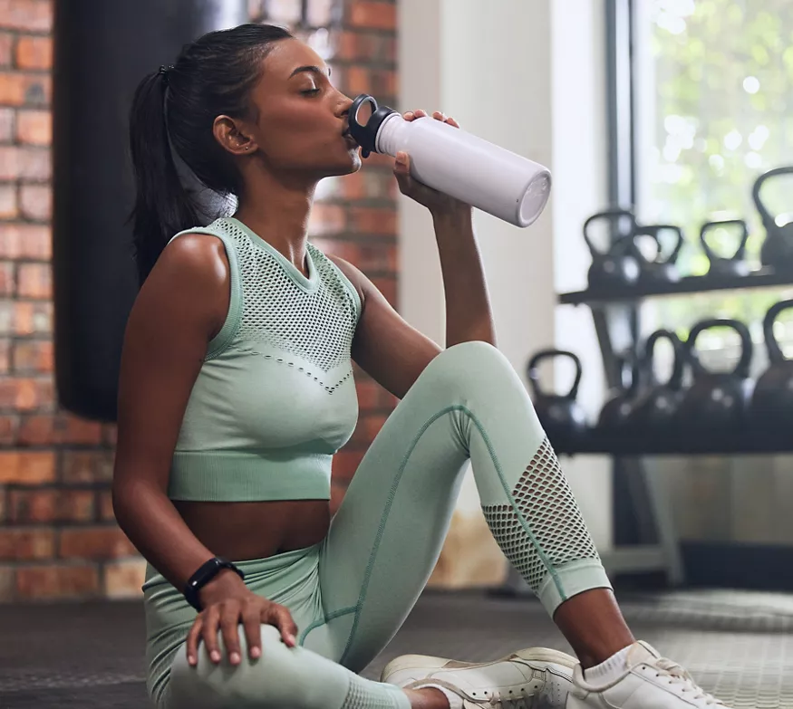Woman drinking out of white bottle while at gym